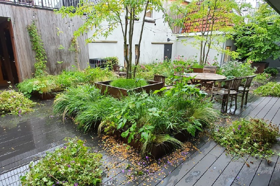 Een groot dakterras met veel groen, een tuintafel met stoelen en bomen die in de speciale boomveerbakken zijn geplant
