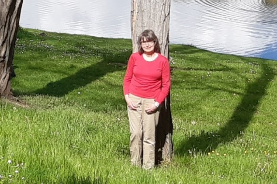 Annette Piepers staat in een rode trui in een grasveld tegen een boom met op de achtergrond water