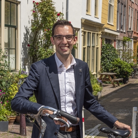 Wethouder gemeente Leiden, Ashley North staat met de fiets in een groene woonwijk