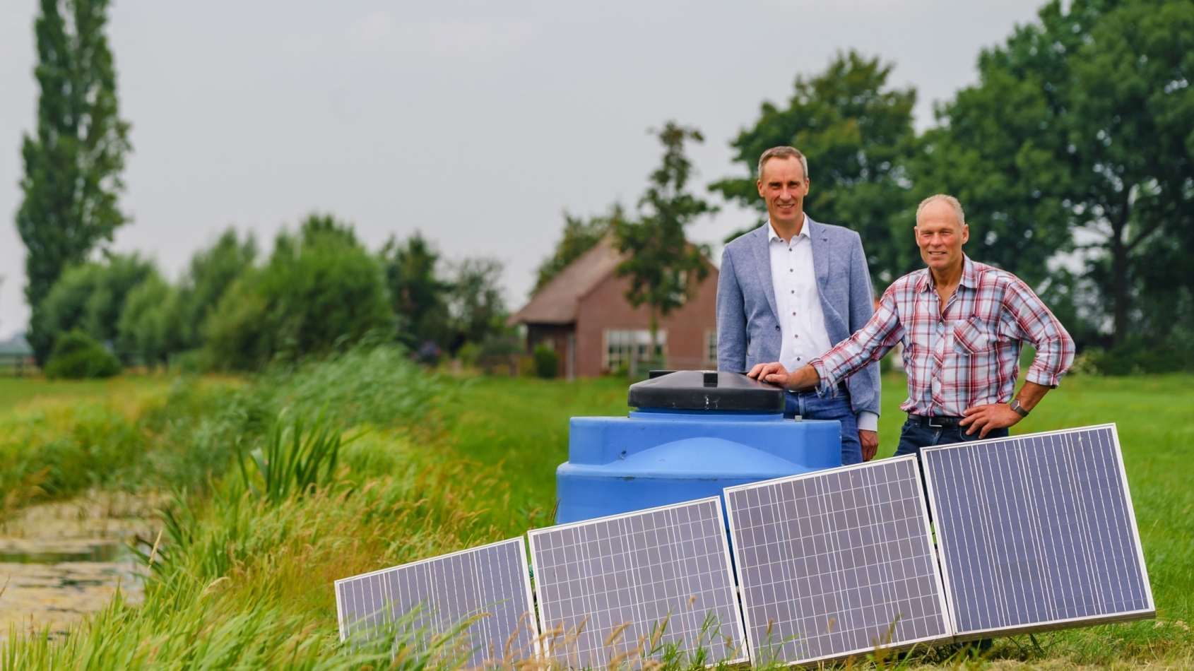 Boer en bankmedewerker staan bij waterpomp en zonnepanelen in wei