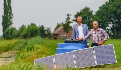 Boer en bankmedewerker staan bij waterpomp en zonnepanelen in wei