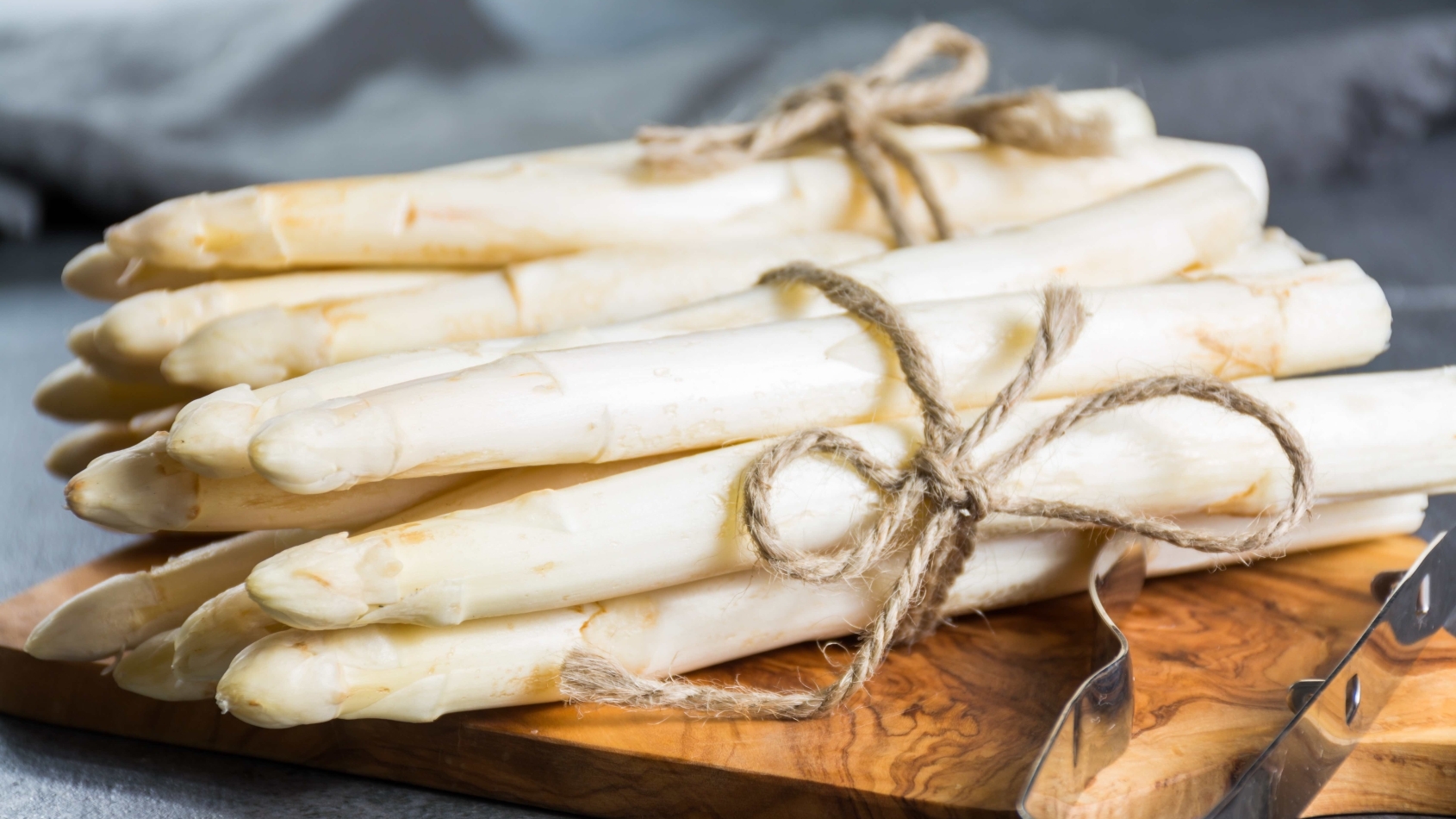 Witte asperges met een touwtje erom op een houten snijplank