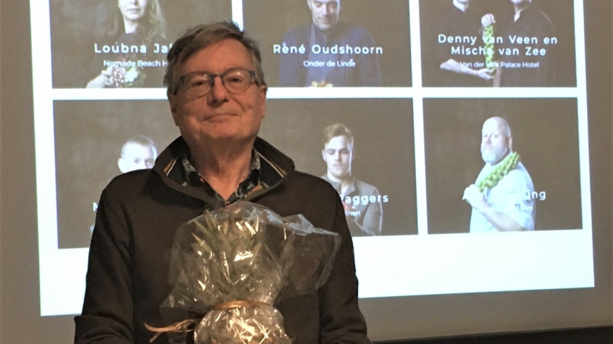 Menko Wiersema met cadeau in handen voor een wand waarop een presentatie te zien is