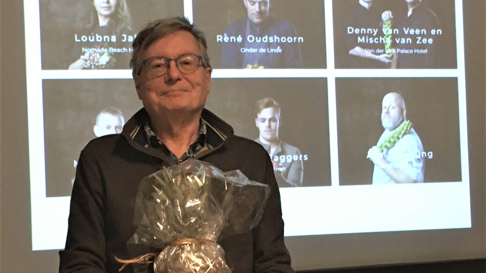 Menko Wiersema met cadeau in handen voor een wand waarop een presentatie te zien is