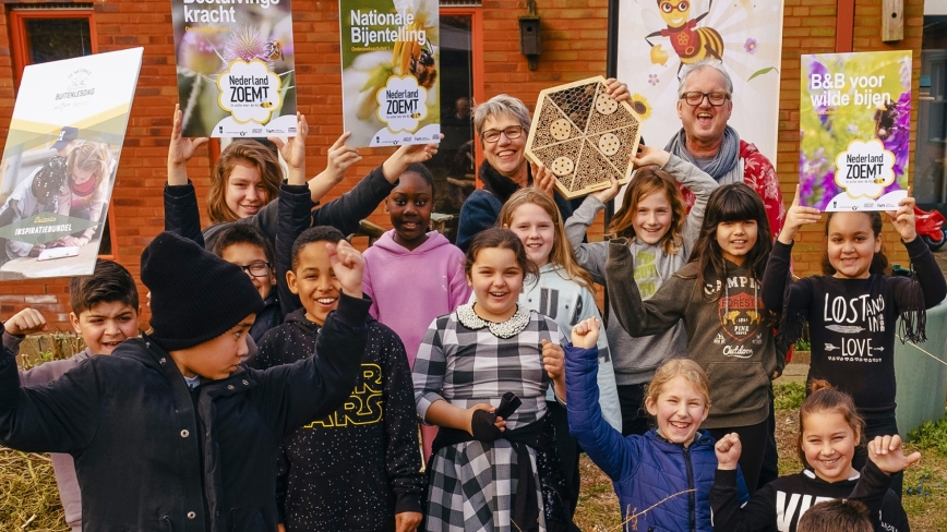 Hannie Korthof staat tussen de schoolkinderen die juichen., Hannie houdt een insectenhotel vast