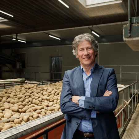 Chairman Farm Frites Piet de Bruijne staat bij aardappelen op een loopband in de fabriek