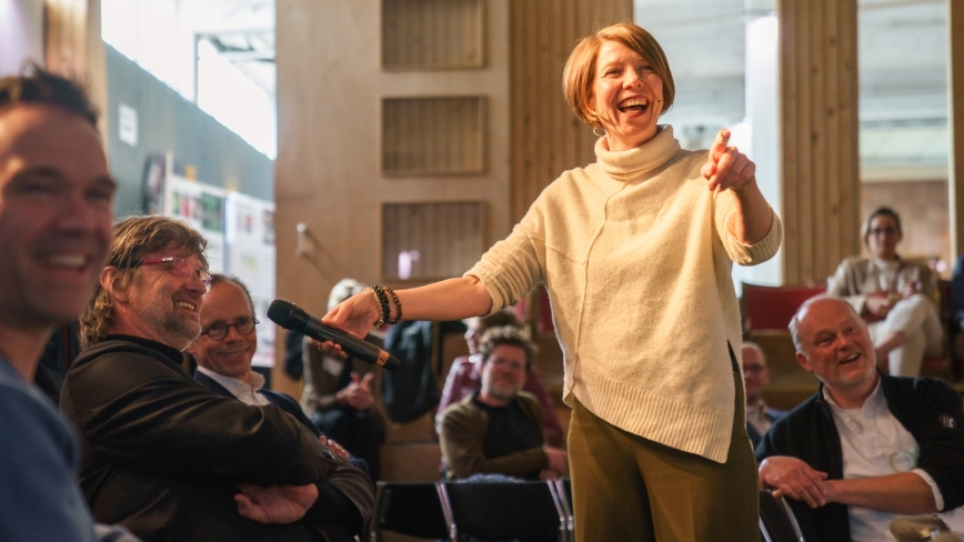 Daphne Teeling lachend met eem microfoon in haar hand voor publiek