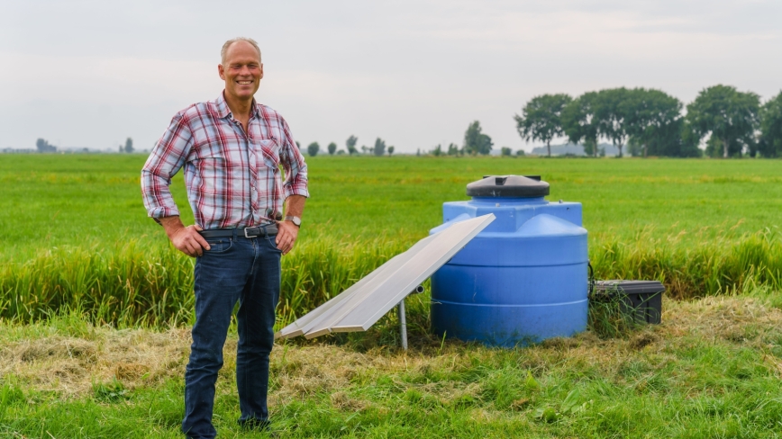 Ad van Rees staat in een weiland bij systeem waterinfiltratie waarvan vooral de grote blauwe ton goed te zien is 