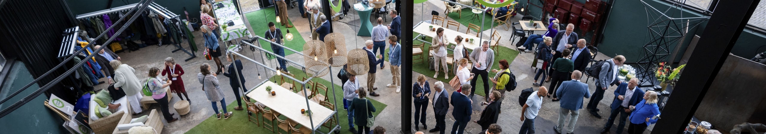 Foto van bovenaf genomen waarop deelnemers van het jubileumevent met elkaar staan te praten in een grote hal