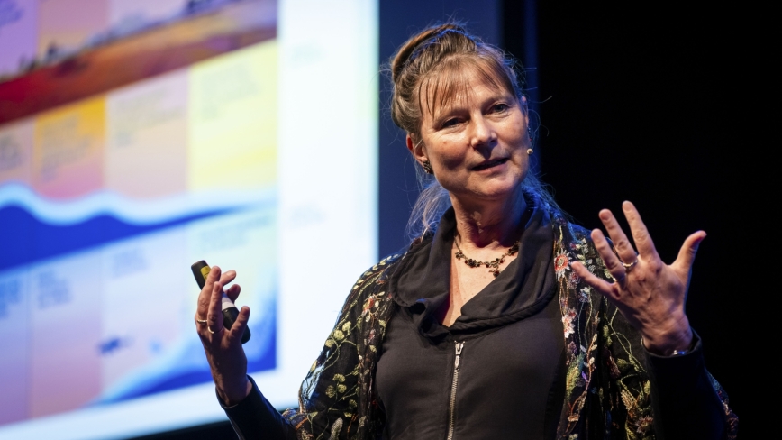 Marjan Minnesma sprekend op een podium, gebarend met haar handen