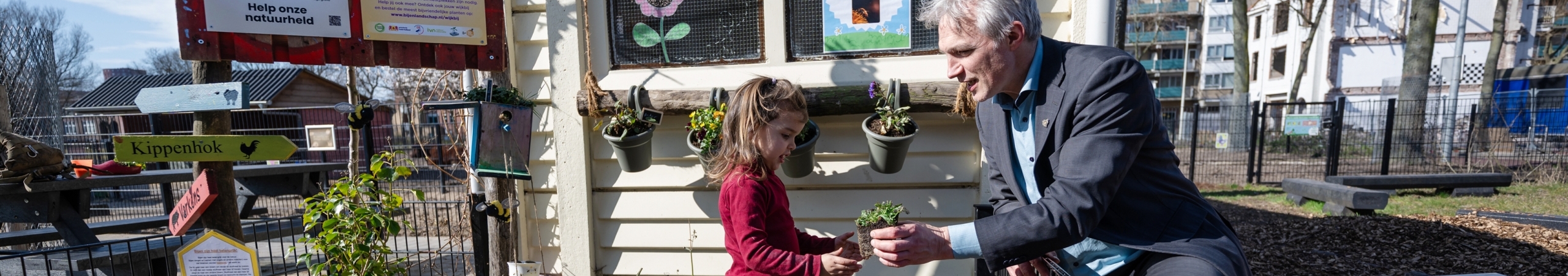 Gedeputeerde Berend Potjer geeft een plantje aan Evineva, een jonge bezoeker van stadsboerderij Molenweide, om een plantje in de grond te zetten in het bij-tanktuintje